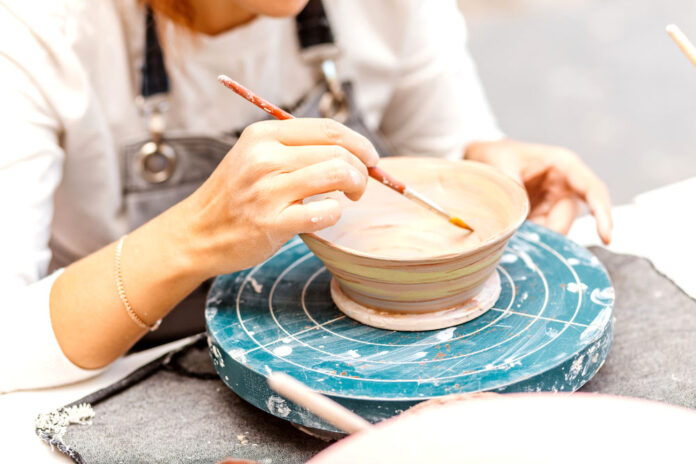A,Woman,Artist,In,Working,Apron,Paints,A,Clay,Pottery